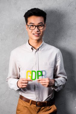 Gülümseyen Asyalı iş adamı elinde renkli GDPR mektupları tutuyor ve kameraya bakıyor. 