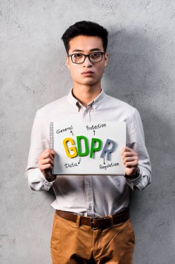 Asyalı işadamı elinde GDPR harfli kağıt tutuyor ve kameraya bakıyor. 