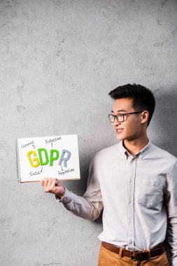 smiling asian businessman holding and looking at paper with gdpr lettering  clipart