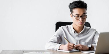 Asya seo yöneticisinin elinde kalem tutarken ve Webinar sırasında dizüstü bilgisayara bakarken panoramik görüntüsü 