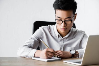 Ofiste Webinar sırasında Asyalı seo yöneticisi deftere yazı yazıyor 