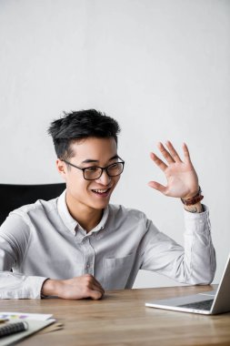 Gülümseyen Asyalı seo yöneticisi Webinar ofiste el sallıyor. 