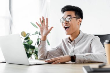 Gülümseyen Asyalı seo yöneticisi Webinar ofiste el sallıyor. 