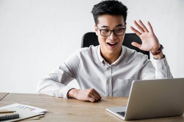 Gülümseyen Asyalı seo yöneticisi Webinar ofiste el sallıyor. 