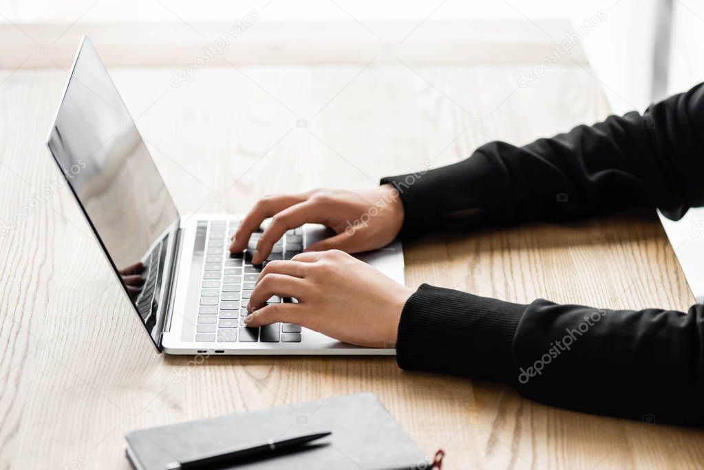 cropped view of hacker sitting at table and using laptop 