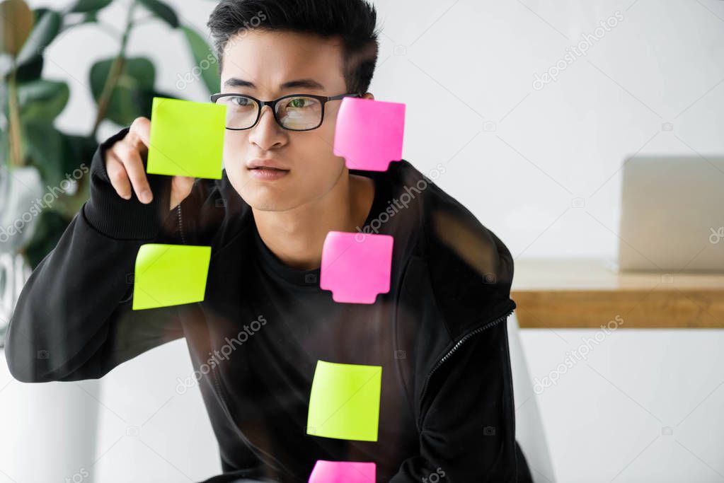 asian seo manager in glasses looking at sticky note on glass 