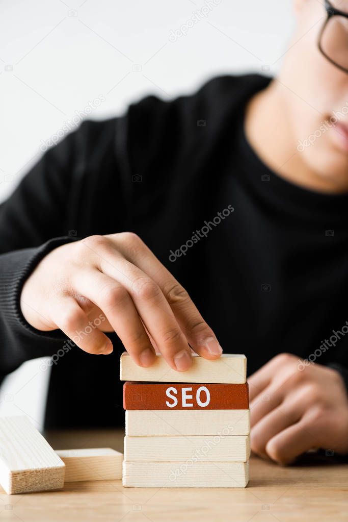 cropped view of seo manager playing with wooden rectangles with lettering seo 