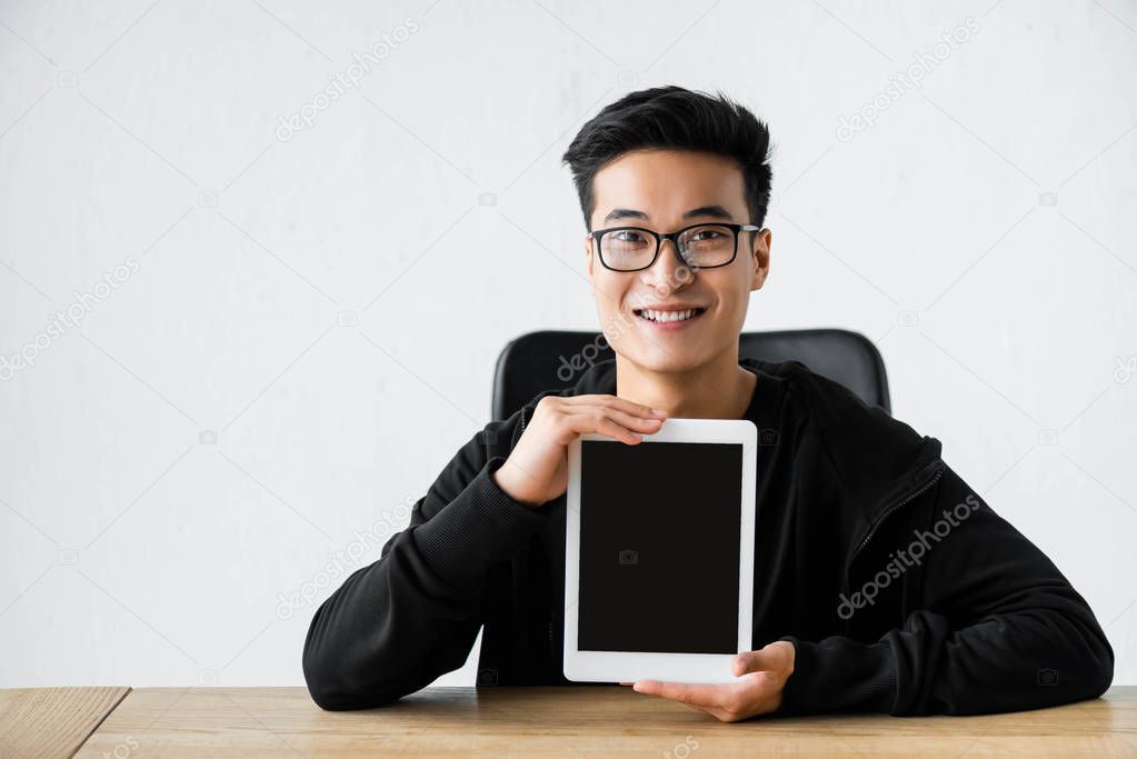 smiling asian hacker holding digital tablet with copy space