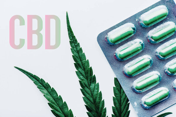 top view of green pills in blister and marijuana leaf on white background with cbd illustration