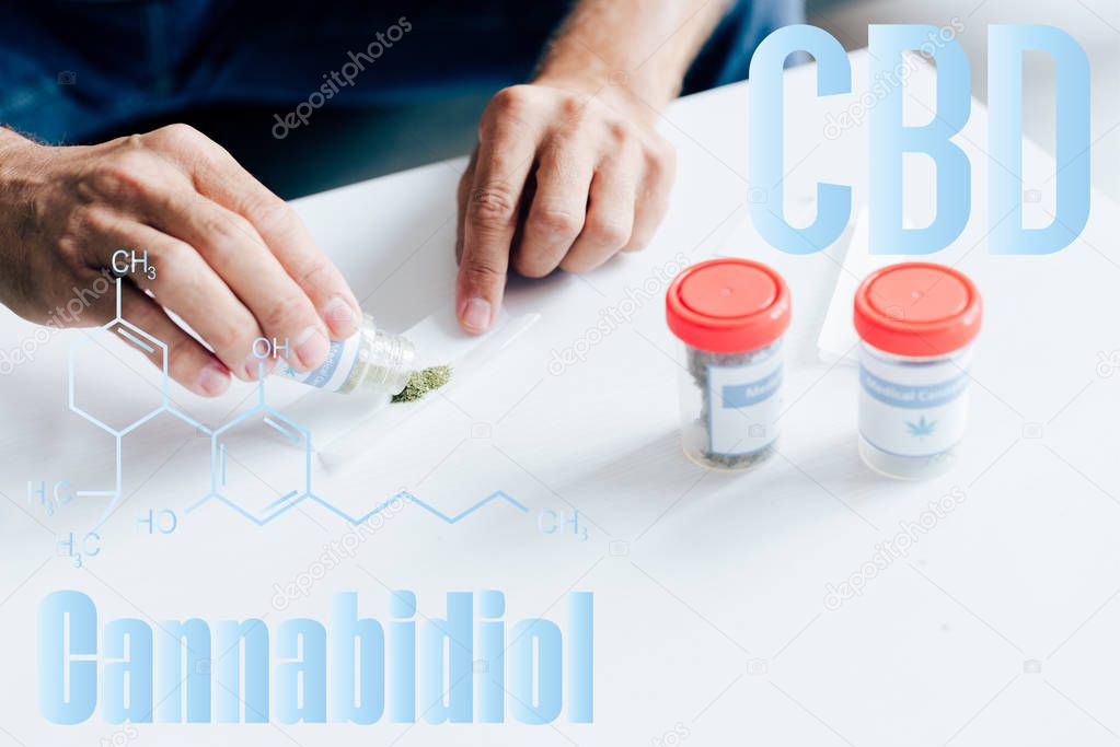 cropped view of man rolling blunt from medical cannabis in apartment with cbd molecule illustration