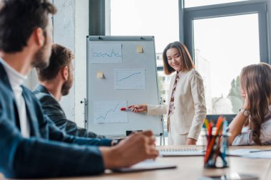 Asyalı konuşmacının seçici odak noktası tablonun yanında duruyor ve meslektaşlarına bakıyor 