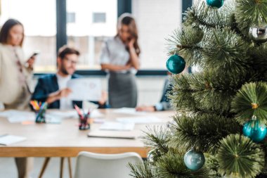 Ofisteki çok kültürlü iş arkadaşlarının yanında dekore edilmiş Noel ağacının seçici odağı  