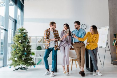 Neşeli iş adamları ve çok kültürlü iş kadınları Noel ağacının yanında şampanya kadehleri kaldırıyorlar. 