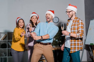 Noel Baba şapkalı mutlu iş adamı şampanya bardaklı çok kültürlü iş arkadaşlarının yanında parti krakeri tutuyor. 