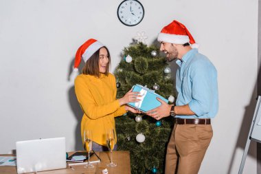 Mutlu sakallı iş adamı, Noel Baba şapkalı Asyalı iş kadınına hediye veriyor. 