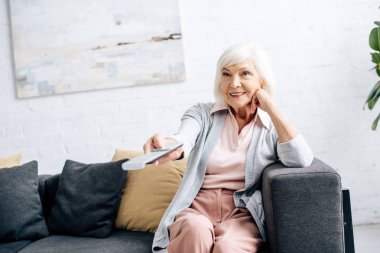 Kanepede oturan ve evde televizyon izleyen gülümseyen bir kadın. 