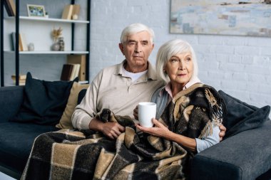 Fincanlı karı koca kanepede oturur ve başka yere bakarlar. 