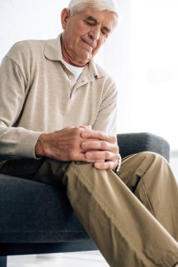 low angle view of senior man sitting on sofa and having knee Arthritis in apartment  clipart