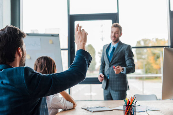 selective focus of businessman raising hand near speaker and businesswoman in office 