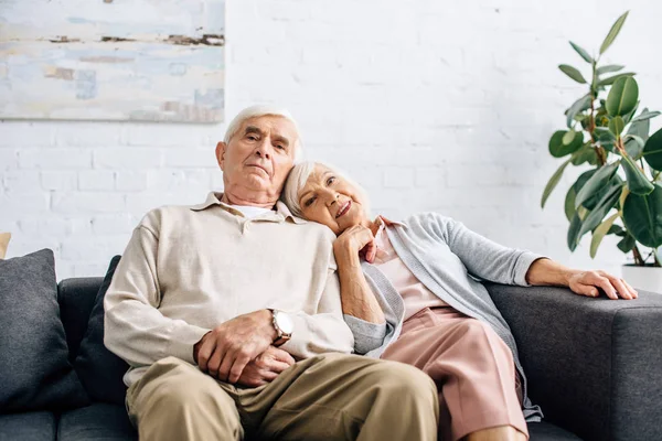 夫と笑顔の妻が肩を並べてアパートのソファに座り — ストック写真