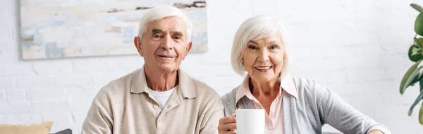 Panoramic Shot Husband Smiling Wife Holding Cup Looking Camera Apartment — Stock Photo, Image