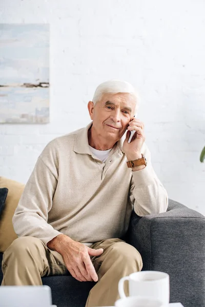 Hombre Mayor Sonriente Sentado Sofá Hablando Teléfono Inteligente Apartamento — Foto de Stock