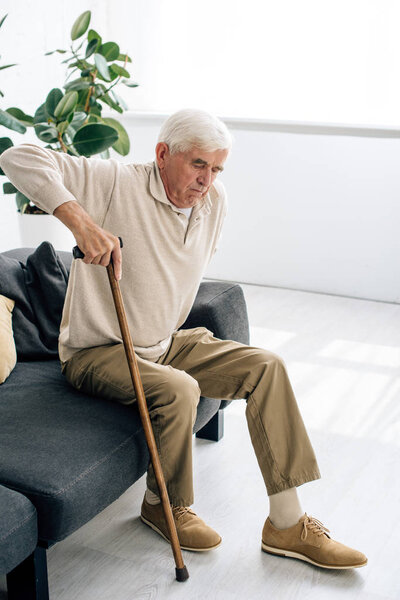 high angle view of senior man sitting on sofa and holding wooden cane in apartment 