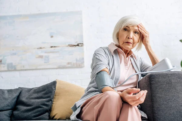 Starsza Kobieta Siedzi Kanapie Mierzy Ciśnienie Krwi Mieszkaniu — Zdjęcie stockowe