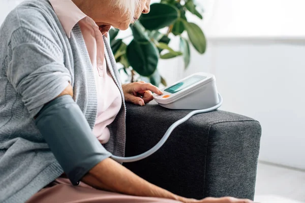 ソファに座って血圧を測定する年配の女性のクロップドビュー — ストック写真