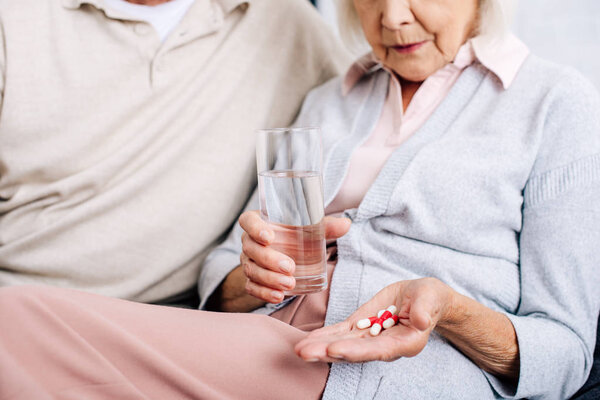 cropped view of husband and wife holding glass and pills in apartment 