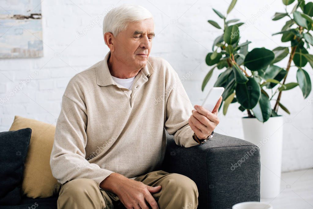 senior man sitting on sofa and using smartphone in apartment 