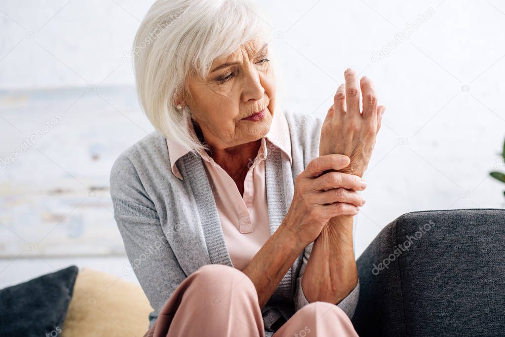senior woman having hand Arthritis and sitting on sofa in apartment 