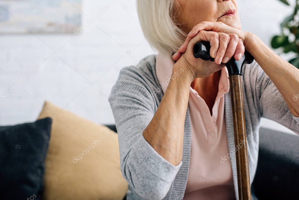 cropped view of senior woman with wooden cane in apartment 