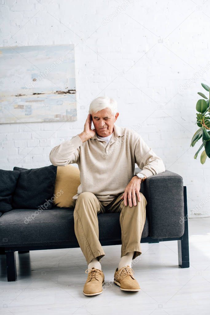 senior man sitting on sofa and having headache in apartment 