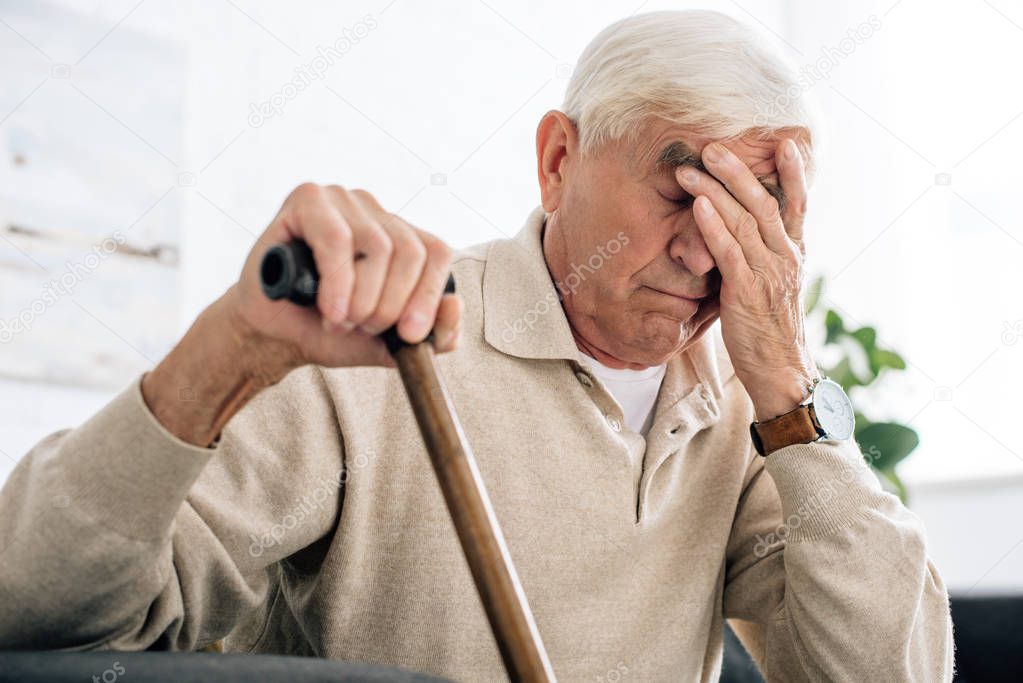 senior man with headache and holding wooden cane in apartment 