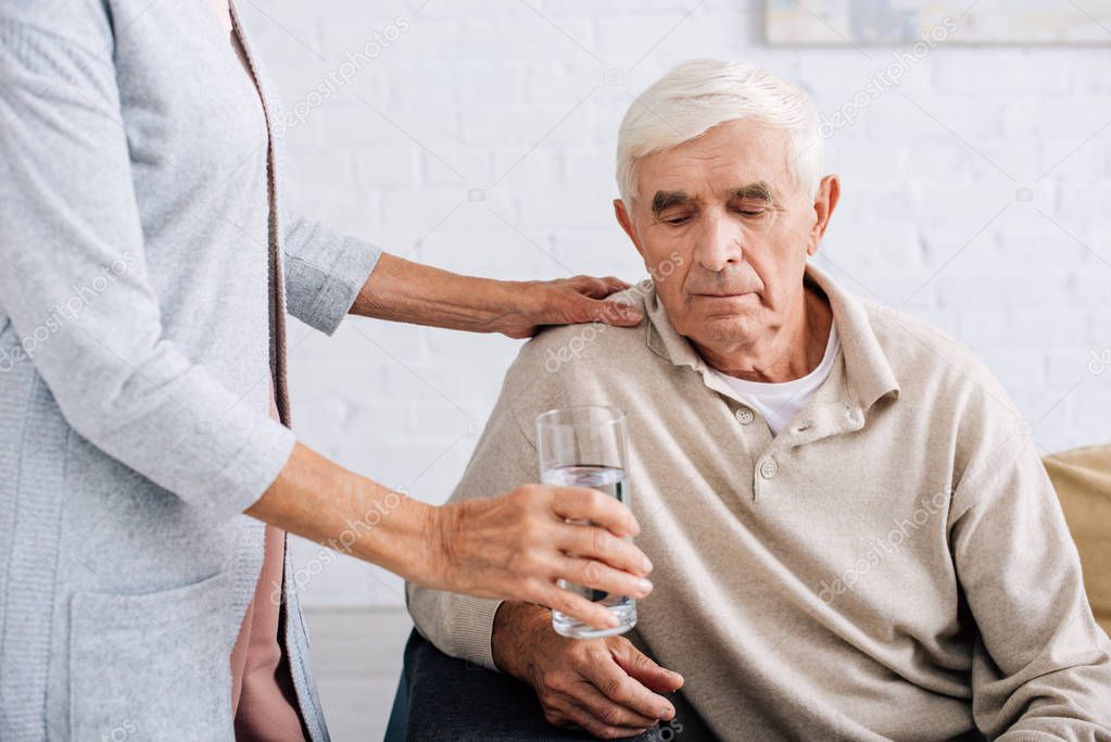 cropped view of wife giving glass of water to husband 