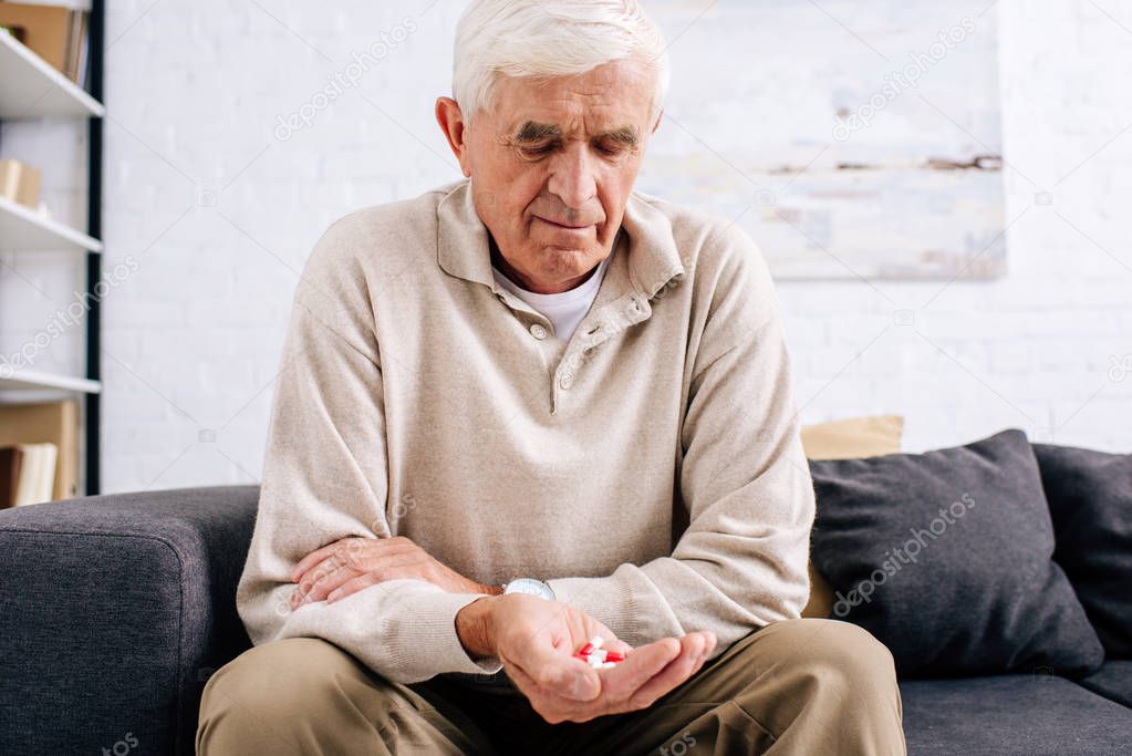 senior man holding pills and sitting on sofa in apartment 