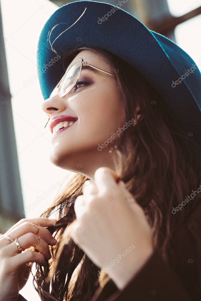 happy stylish girl posing in eyeglasses and hat on urban roof