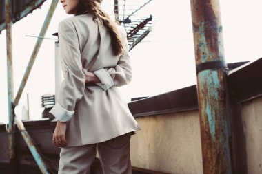 Kentin çatısında bej takım elbiseli şık bir kadının kırpılmış görüntüsü.