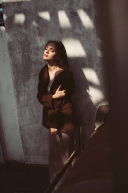 İpek elbise ve çatıda kahverengi ceket giymiş zarif bir manken.