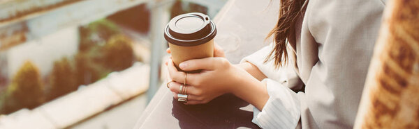cropped view of trendy girl in beige suit posing on roof with coffee to go