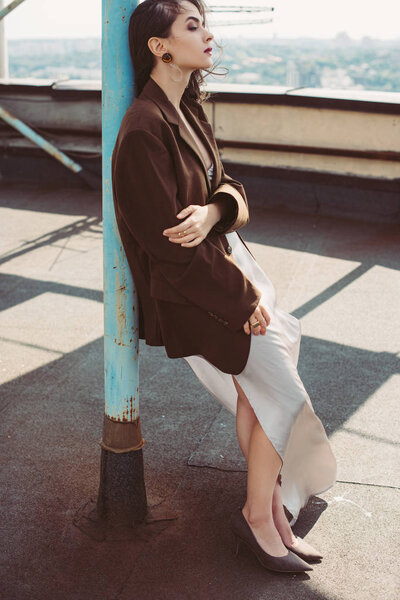 beautiful fashionable girl posing in silk dress and brown jacket on roof