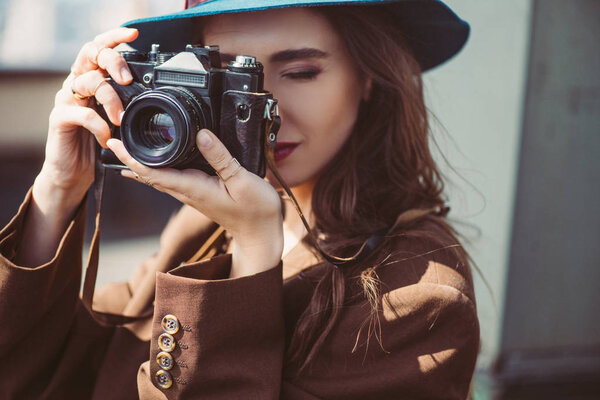 attractive woman in hat taking photos on retro photo camera on roof