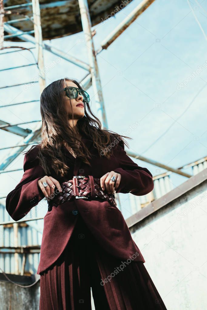 fashionable model posing in trendy burgundy suit and sunglasses on urban roof 