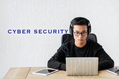 Asyalı hacker dizüstü bilgisayar kullanıyor ve siber güvenlikle illüstrasyonun yanında oturuyor 