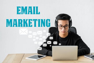 Asyalı seo yöneticisi dizüstü bilgisayar kullanıyor ve e-posta simgeleri ve pazarlama harfleriyle illüstrasyonun yanında oturuyor 