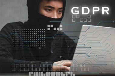 Asyalı hacker dizüstü bilgisayar kullanıyor ve GDPR illüstrasyonunun yanında oturuyor 