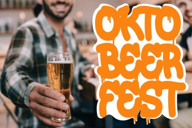 Oktobeerfest illüstrasyonunda arkadaşlarıyla barda otururken elinde bir bardak light bira tutan adamın seçici odak noktası.