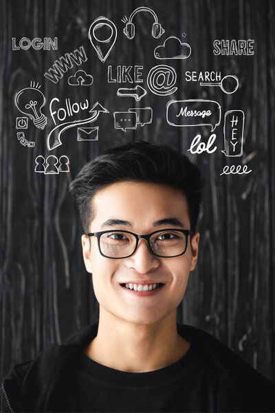 улыбающийся азиат в очках смотрит на камеру на деревянном фоне с иллюстрацией
  