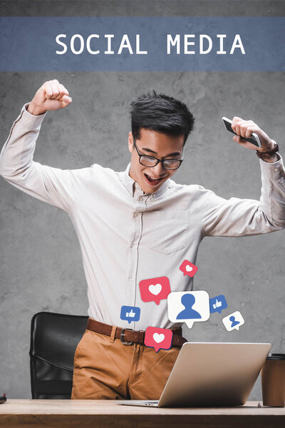 happy asian seo manager showing yes gesture and standing near social media illustration